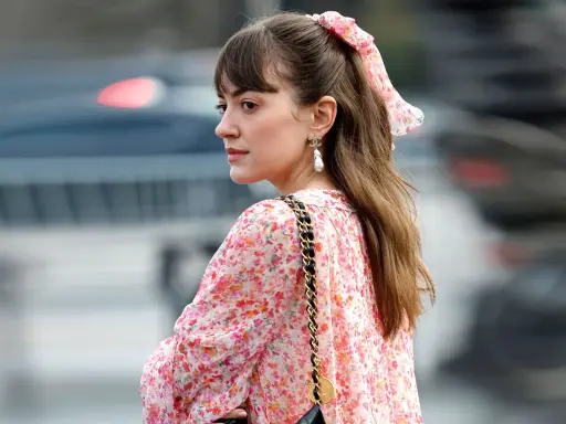 Eine Frau mit einem Blumenkleid und einer einfachen Frisur, perfekt für eine Hochzeitsgast. Ein Scrunchie mit Blumenmuster ziert ihren Pferdeschwanz.