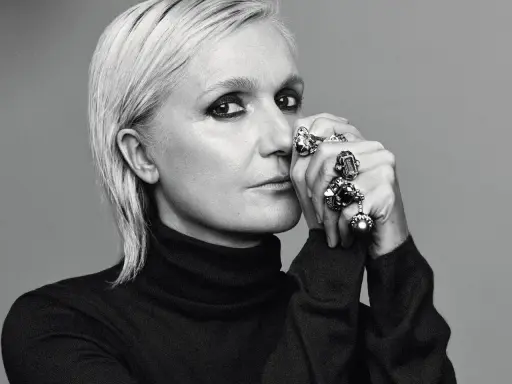 Maria Grazia Chiuri, mit markantem Make-up und vielen Ringen, blickt nachdenklich in die Kamera.