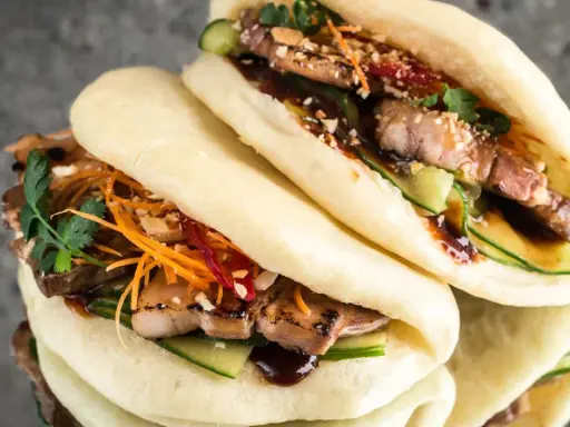 Saftige bao buns mit gegrilltem Fleisch, Gurke, Karottenstreifen und Koriander. Ein Genuss für alle Sinne!