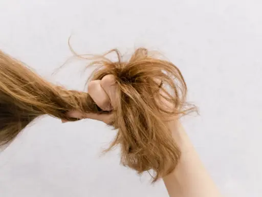 Eine Hand greift nach strohigen Haaren, die trocken und ungepflegt aussehen.