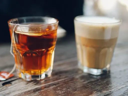Ein Glas Tee mit Beutel und ein Latte Macchiato stehen nebeneinander. Eine leckere alternative zu Kaffee.