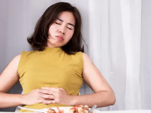 Frau mit schmerzverzerrtem Gesicht hält sich den Bauch. Sie leidet unter Bittertropfen vor oder nach dem Essen.