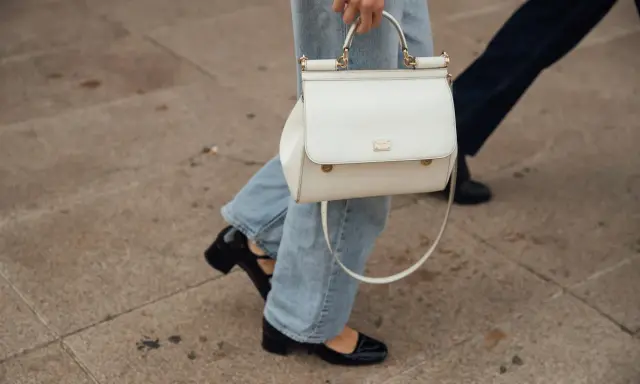 Eine Frau kombiniert lässig wide leg jeans mit schwarzen Lackschuhen und einer weißen Handtasche.