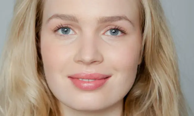Blonde Frau mit blauen Augen und rosafarbenen Lippen, die frisch aussieht.