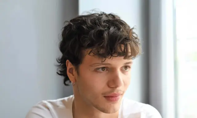 Junger Mann mit lockigem, kurzem Mullet-Haarschnitt und einem dezenten Ringohrring.