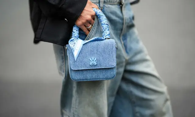 Ein hellblaues Jeans-Täschchen mit einem quadratischen Tuch binden, das den Griff ziert. Das Tuch hat ein Paisleymuster und den Schriftzug "AMIRI".