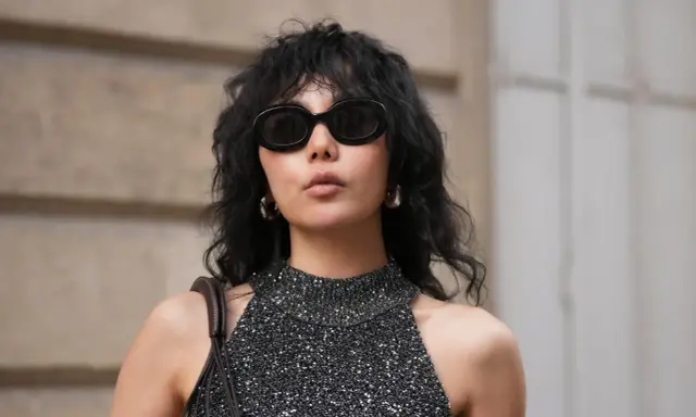Frau mit schwarzem Wolf Cut Locken, Sonnenbrille und glitzerndem Top.