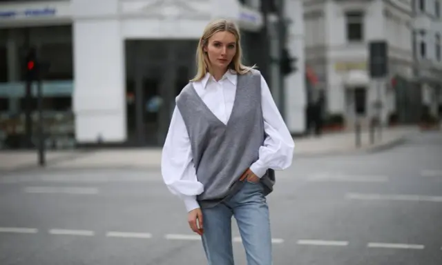 Stylische Frau in grauem Pullunder, weißer Bluse und Jeans. So lässt sich ein Pullunder kombinieren für einen lässigen Look.
