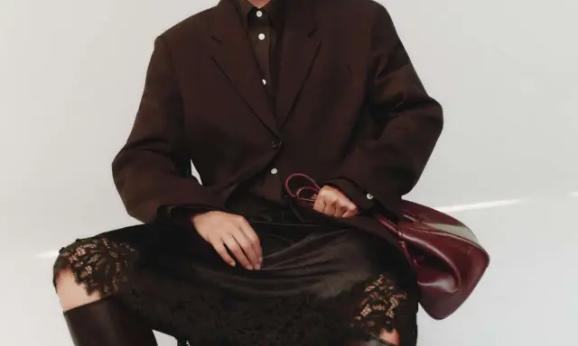 Elegant outfit: braun und schwarz kombinieren mit einem braunen Blazer, schwarzer Spitzenrock und Lederstiefel. Eine Hand hält eine weinrote Tasche.