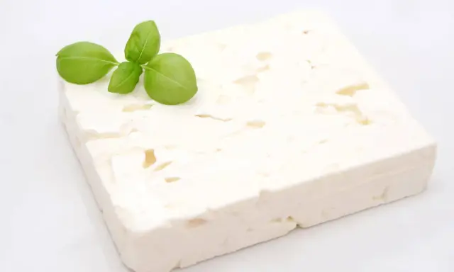 Ein Block Feta-Käse mit Basilikumblättern. Ist Feta gesund? Ja, er liefert Kalzium und Proteine.