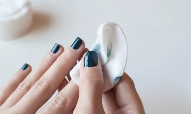 Eine Hand mit dunkelblauem Nagellack wird mit einem Wattepad abgewischt, um den Nagellack zu entfernen.
