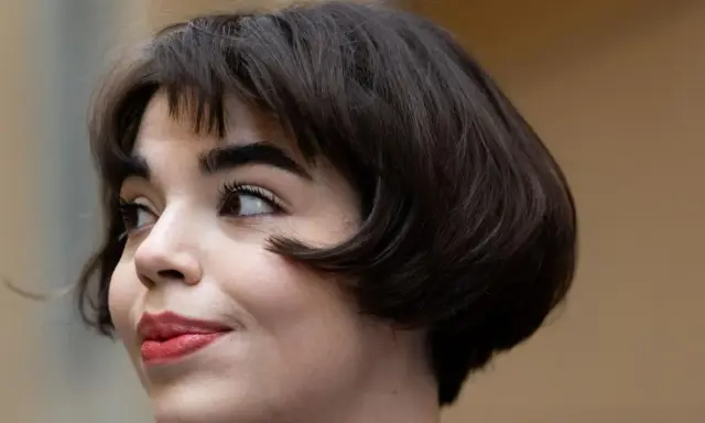 Eine Frau mit einem eleganten, dunklen short bob und rotem Lippenstift blickt nach links.