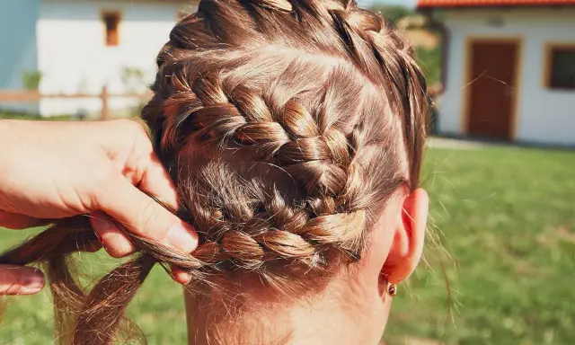 Zopf flechten für Oktoberfest Frisuren einfach. Eine Hand flechtet das braune Haar zu einem kunstvollen Zopf.