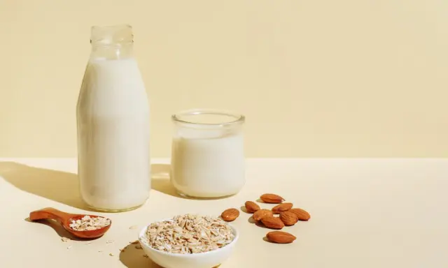 Flasche und Glas mit milchigem Getränk, daneben Mandeln und Haferflocken. Ob Mandelmilch oder Hafermilch, die Wahl ist leicht.