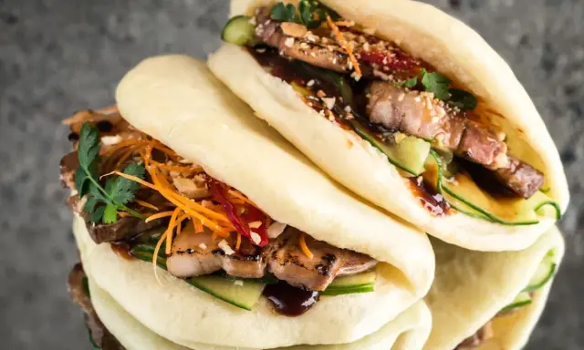 Saftige bao buns mit gegrilltem Fleisch, Gurke, Karottenstreifen und Koriander. Ein Genuss für alle Sinne!