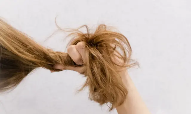 Eine Hand greift nach strohigen Haaren, die trocken und ungepflegt aussehen.