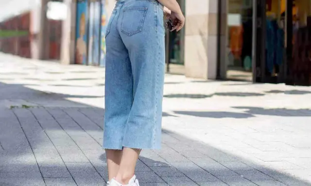 Styling culotte jeans: Ein lässiger Look mit hellblauen Jeans, weißem Shirt und Sneakern auf gepflastertem Weg.