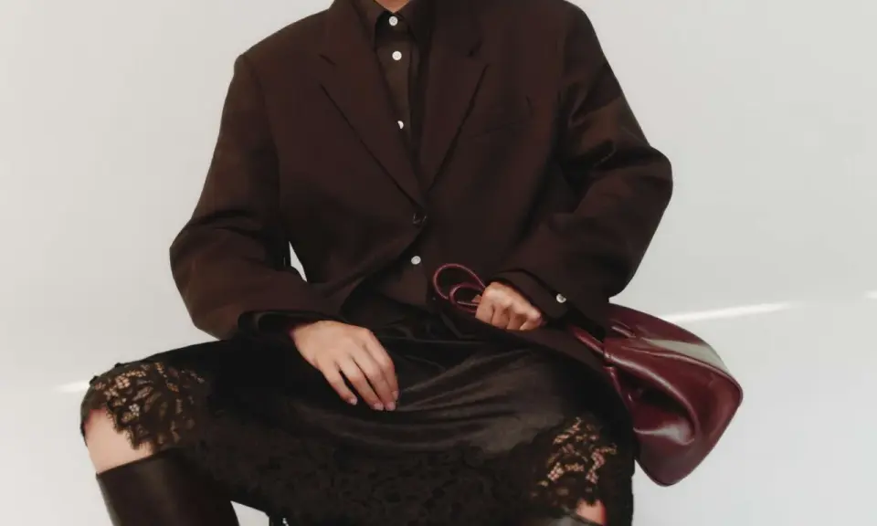 Elegant outfit: braun und schwarz kombinieren mit einem braunen Blazer, schwarzer Spitzenrock und Lederstiefel. Eine Hand hält eine weinrote Tasche.