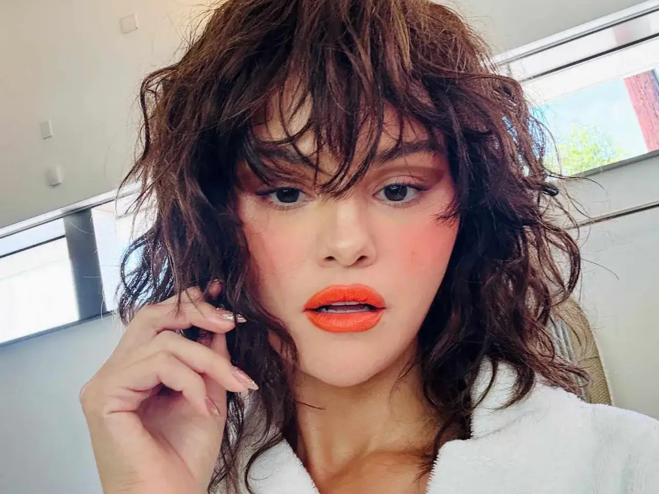 Selena Gomez mit ihrem neuen Butterfly Cut, leuchtend orange Lippen und rosafarbenem Rouge.
