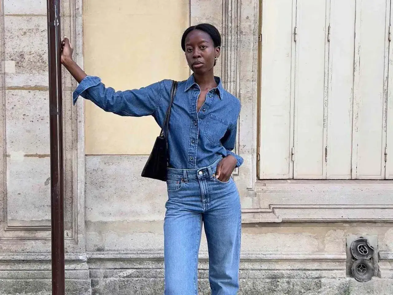 Frau in Jeanshemd und wide leg jeans kombinieren sie lässig mit einer schwarzen Tasche. Ein urbaner Look.