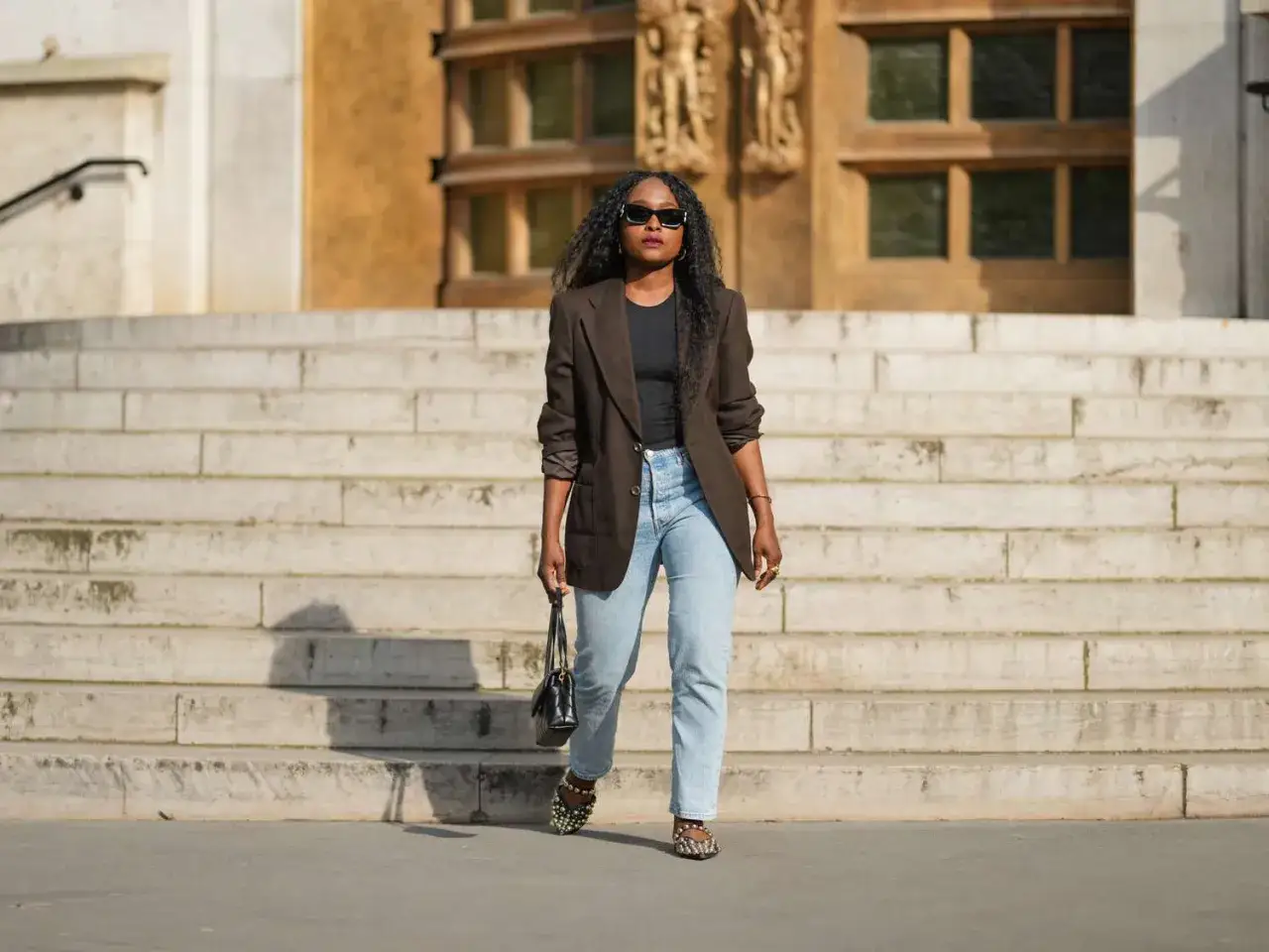 Frau in braunem Blazer und hellblauen Mom Jeans kombiniert mit auff&auml;lligen Schuhen und Tasche.