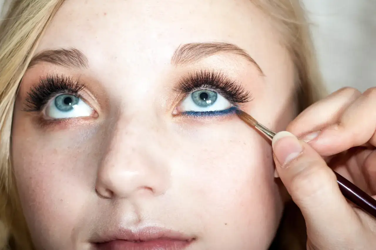 Ein Pinsel tr&auml;gt blauen Eyeliner auf die untere Wasserlinie des blauen Auges auf.