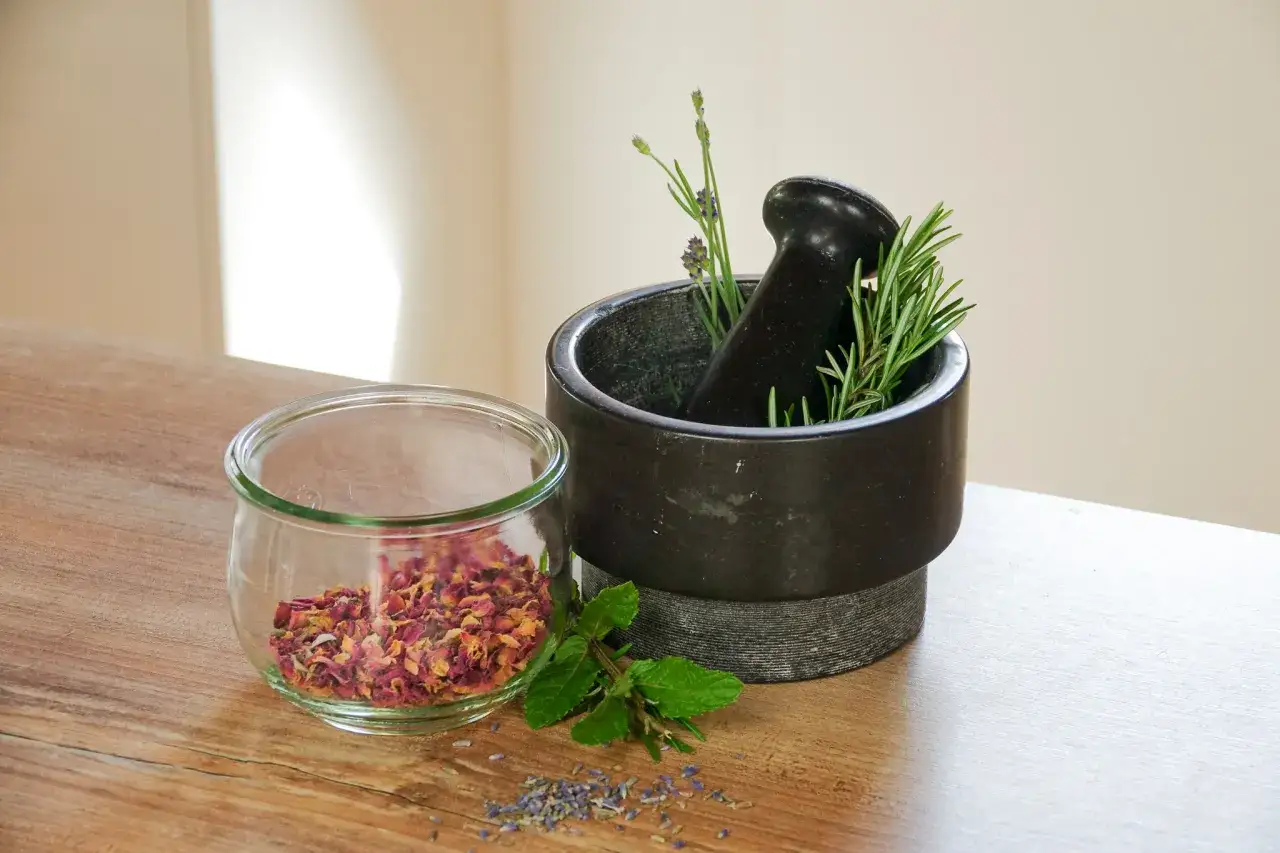 M&ouml;rser mit Rosmarin und Lavendel, daneben ein Glas mit Rosenbl&auml;ttern. Perfekt f&uuml;r naturkosmetik selber machen.
