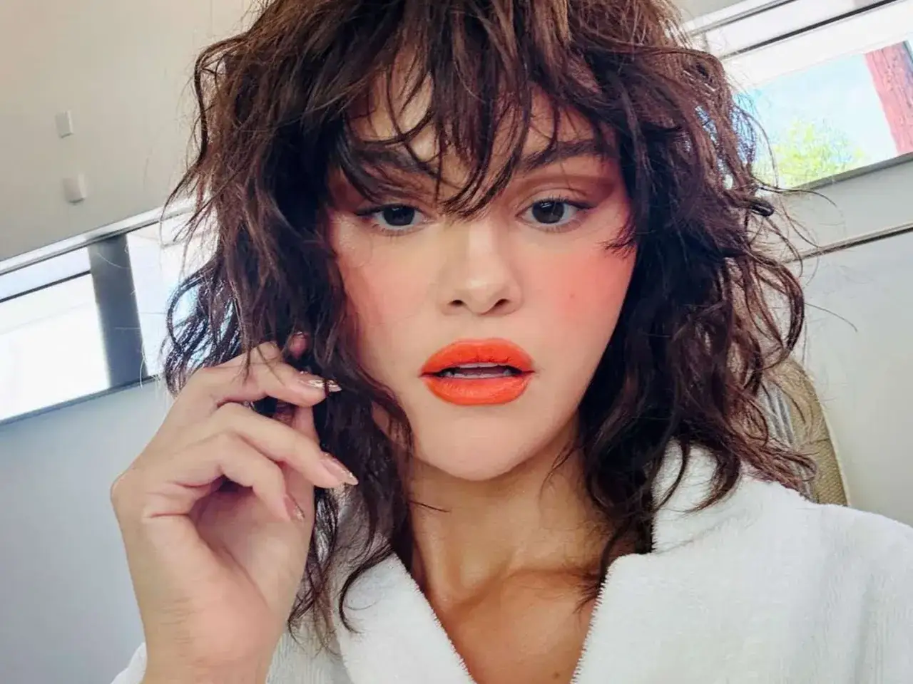 Frau mit braunem Wolf Cut und Locken, leuchtend orange Lippen und rosafarbenem Rouge.