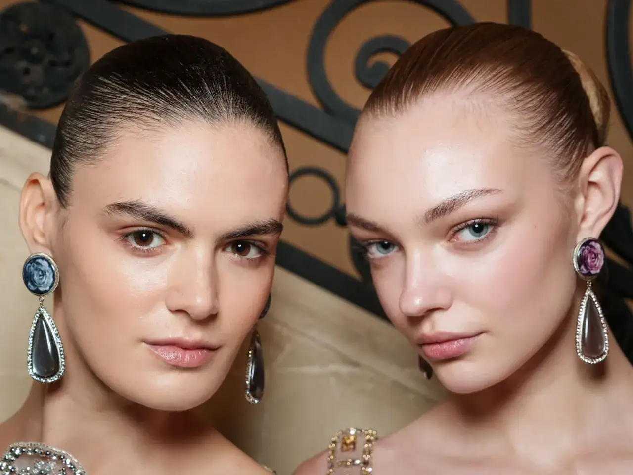 Zwei Models mit glatten Haaren und geraden Augenbrauen, die auffälligen Schmuck tragen.