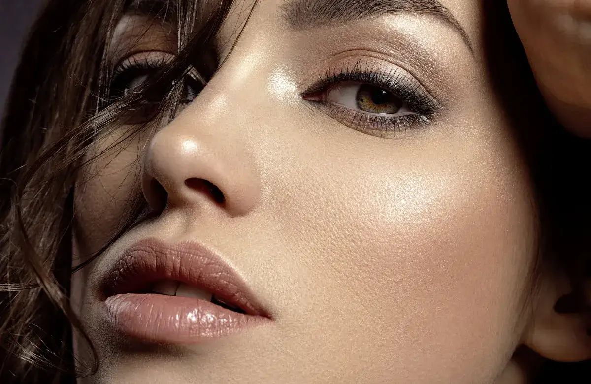 Nahaufnahme eines Gesichts mit dezenten smokey eyes, gl&auml;nzenden Lippen und einem warmen Hautton.