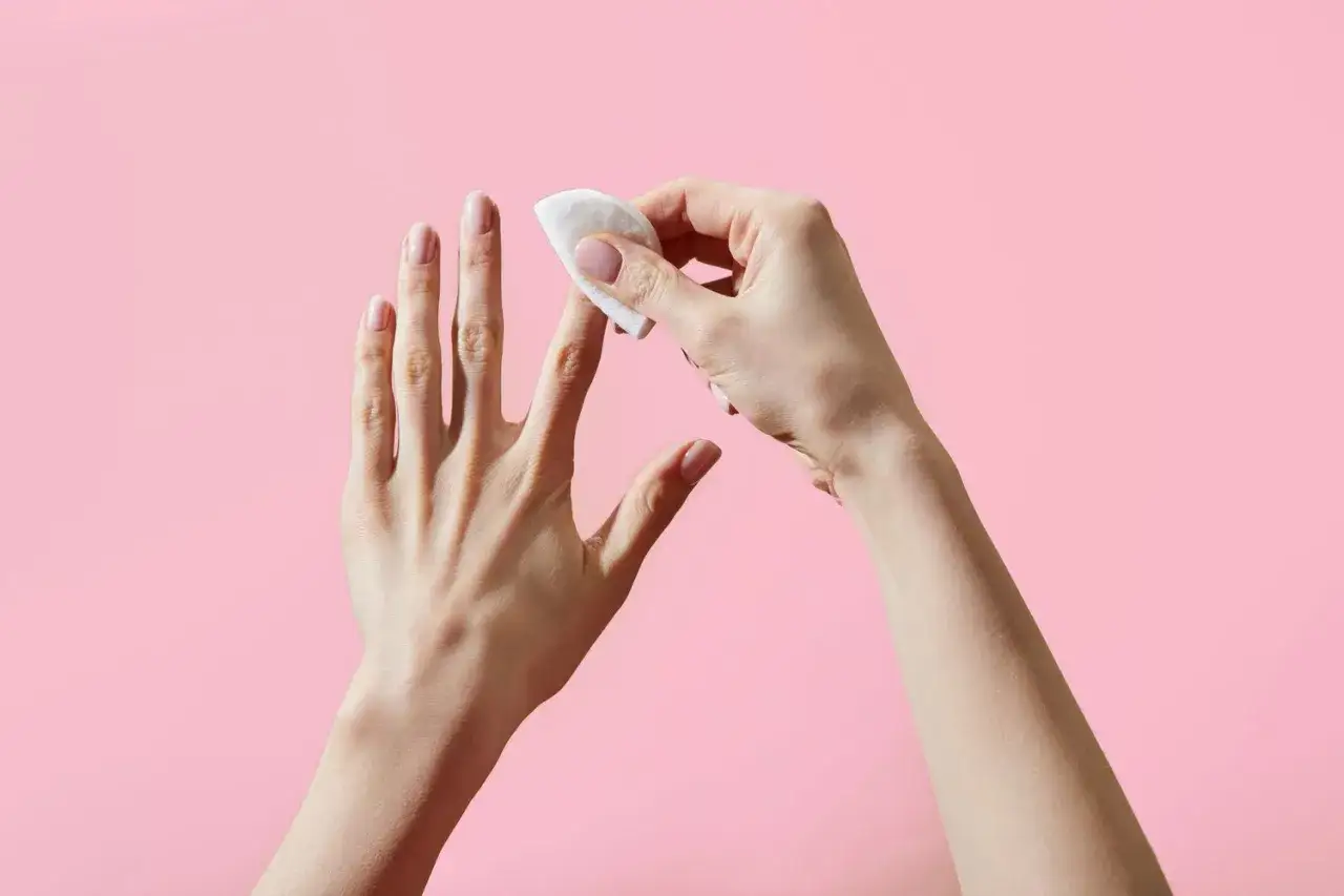 H&auml;nde mit Wattepad und Nagellackentferner, um den Nagellack zu entfernen.