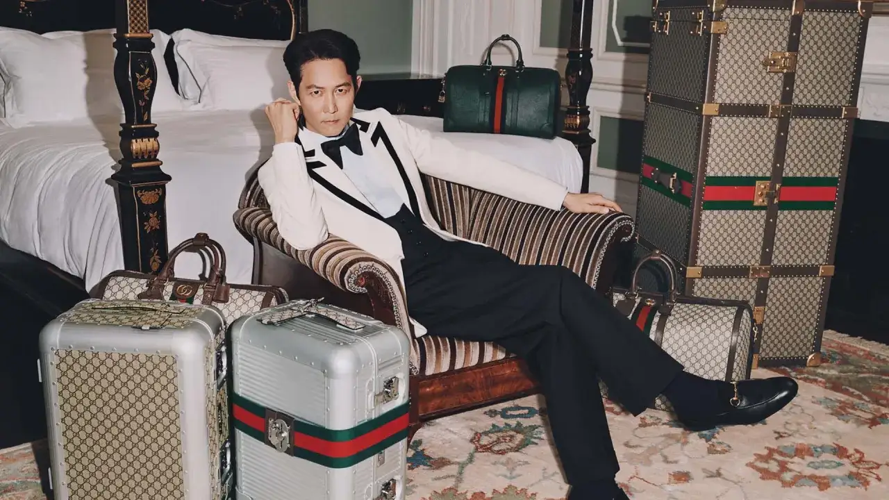 Ein Mann in einem eleganten wei&szlig;en Anzug sitzt umgeben von Gucci-Gep&auml;ck. Der Gucci designer hat hier ein luxuri&ouml;ses Reise-Ensemble geschaffen.
