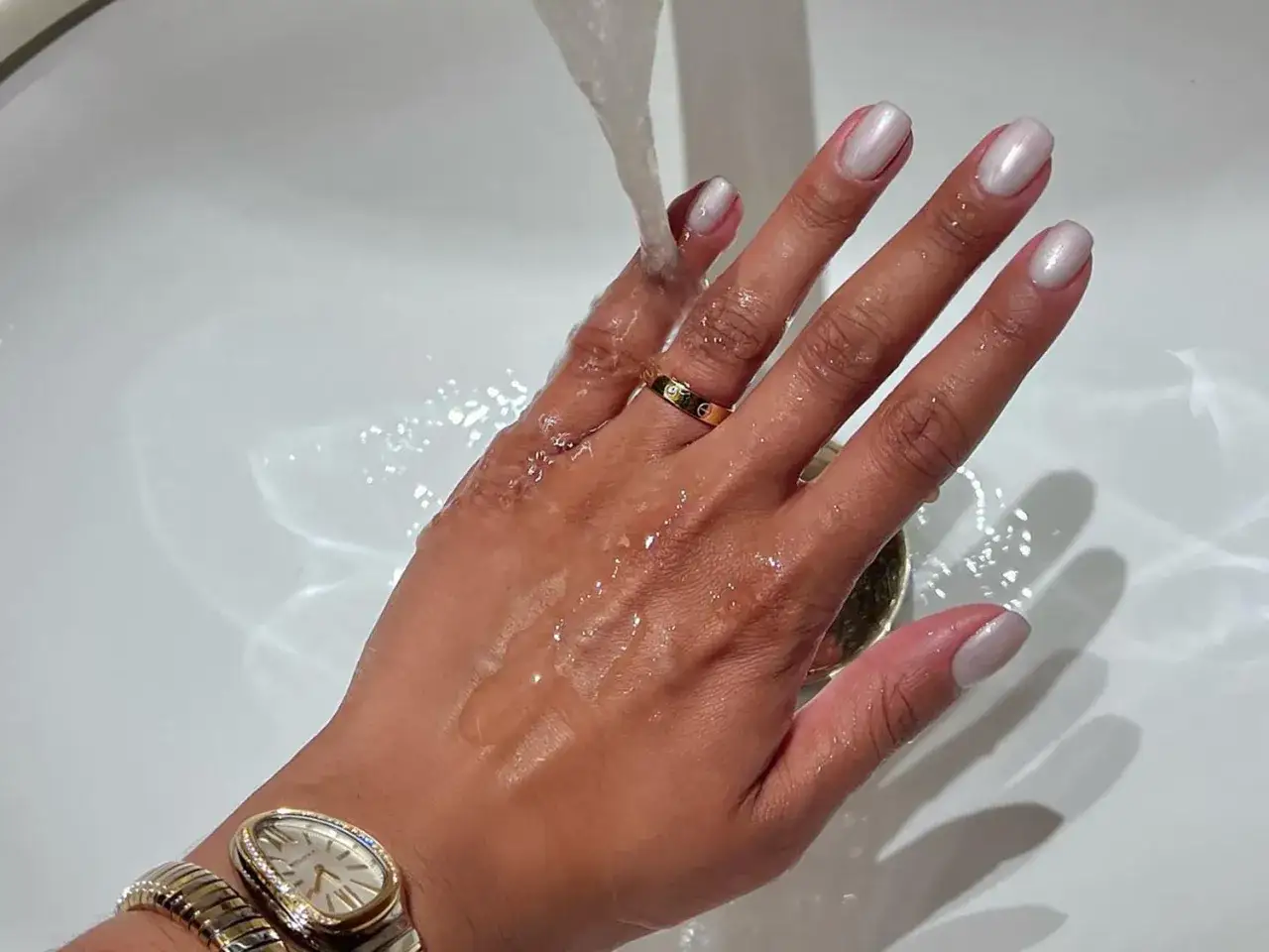 Hände mit frisch lackierten Nägeln unter fließendem Wasser. Die Frage
