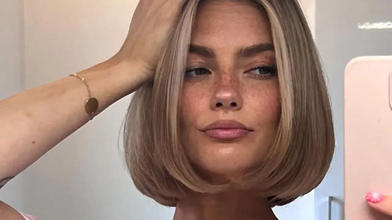 Frauenkopf mit einem stilvollen short bob und Sommersprossen. Eine Hand ber&uuml;hrt das Haar, w&auml;hrend sie in die Kamera blickt.