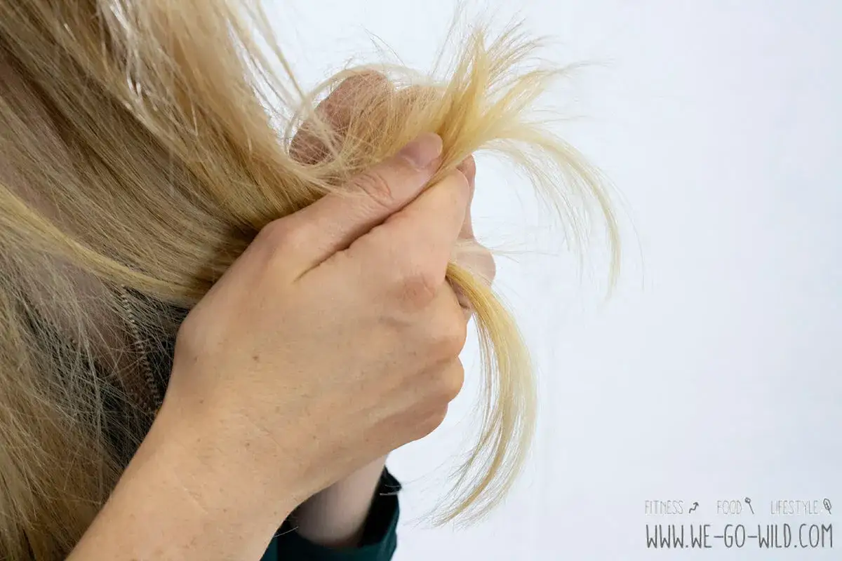 Eine Hand hält blonde Haare, die nach einer Haarmaske vor dem Waschen ins trockene Haar noch etwas strohig aussehen.