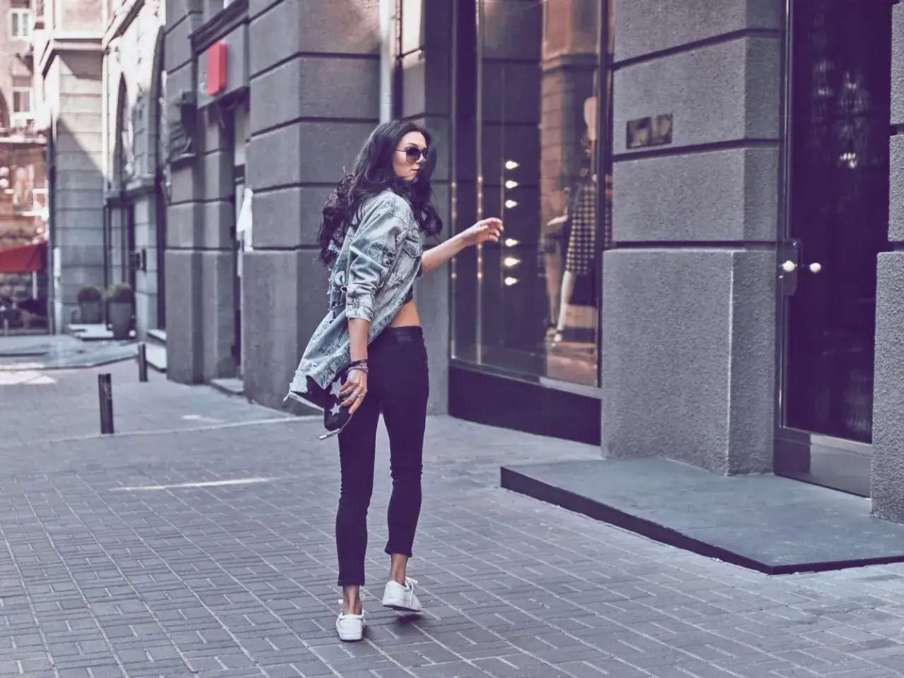 Stylische Frau in schwarzer Stoffhose und Jeansjacke, die l&auml;ssig durch die Stadt schlendert.