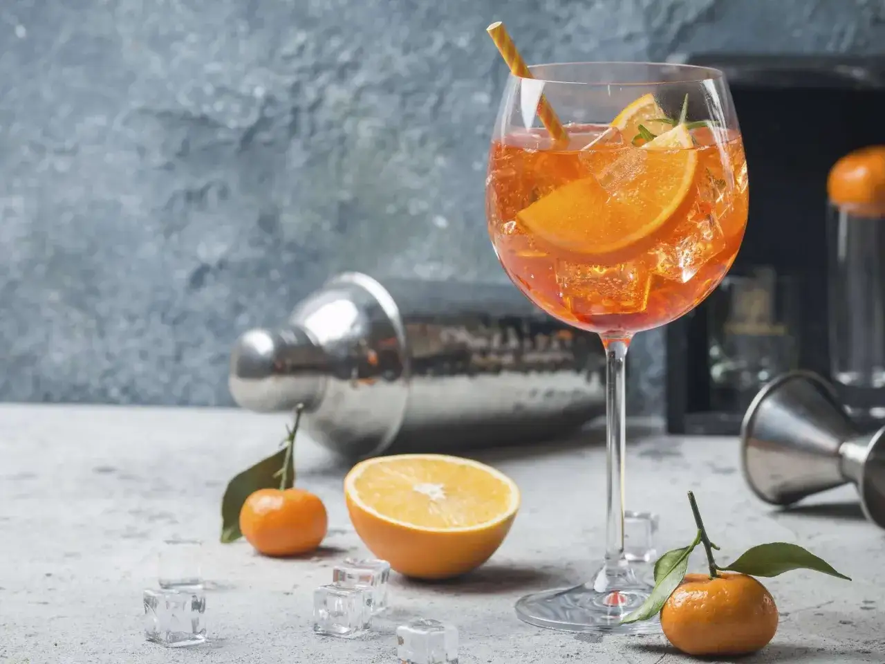 Erfrischender Aperol Spritz mit Orangenscheiben und Eiswürfeln. Die spritz zutaten der iba sind perfekt arrangiert, daneben ein Shaker und Jigger.