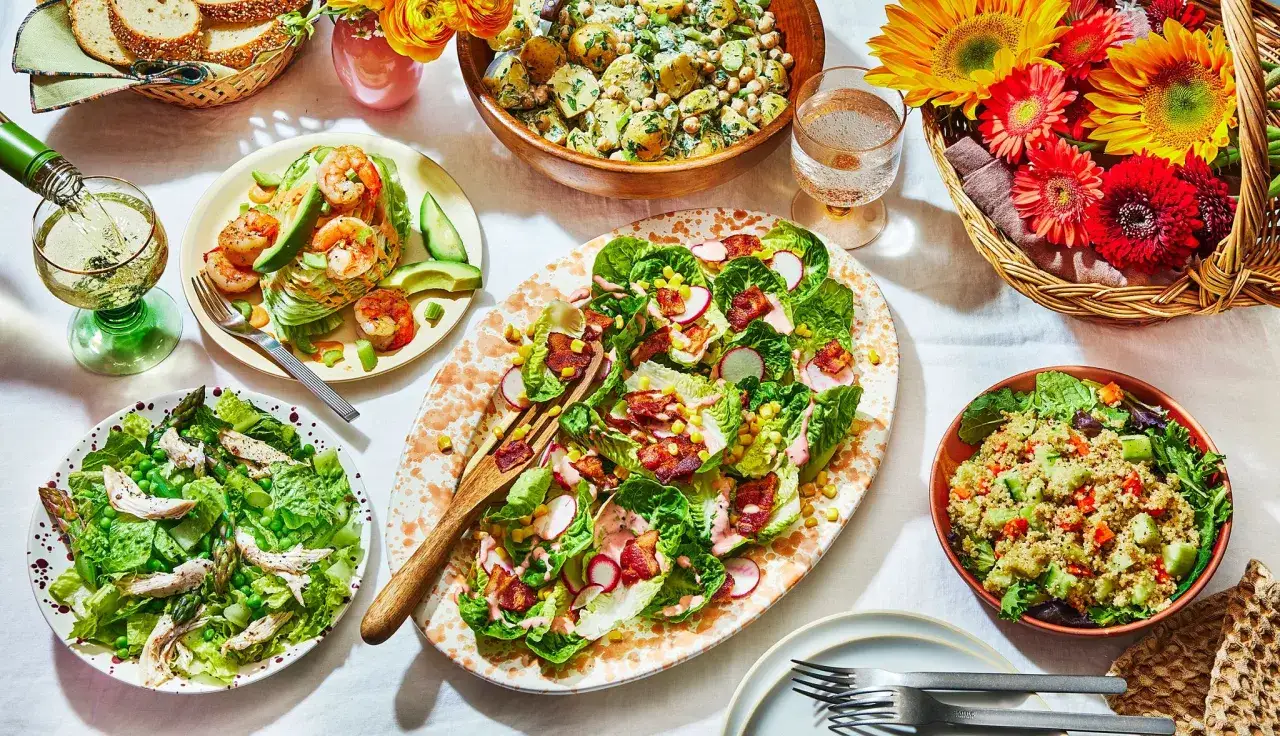 Leichtes Essen im Sommer: Salate mit Garnelen, Hähnchen, Quinoa und Kartoffelsalat, dazu Brot und Blumen.