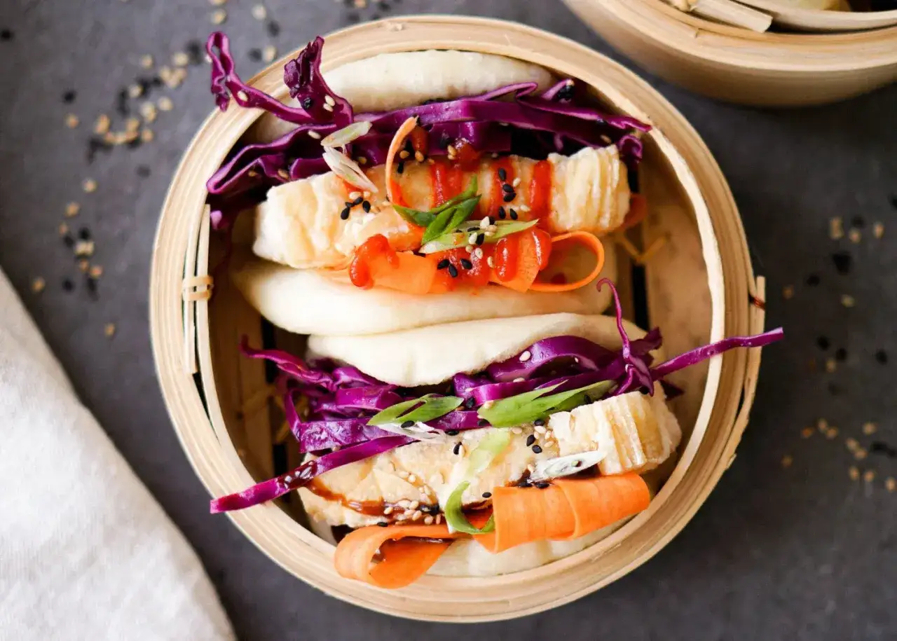 Ged&auml;mpfte bao buns gef&uuml;llt mit Rotkohl, Karottenstreifen, Fr&uuml;hlingszwiebeln und einem Hauch Sriracha.