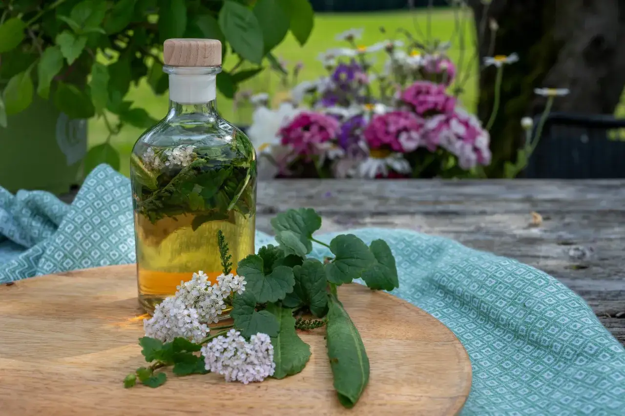 Flasche mit Kr&auml;utertinktur, ideal als Bittertropfen vor oder nach dem Essen. Daneben frische Kr&auml;uter und Bl&uuml;ten auf einem Holzteller.