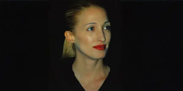 Frau mit blondem Pferdeschwanz und rotem Lippenstift, im **Carolyn Bessette-Kennedy Style**, blickt nach rechts.