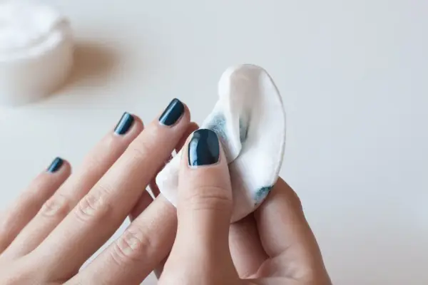 Eine Hand mit dunkelblauem Nagellack wird mit einem Wattepad abgewischt, um den Nagellack zu entfernen.