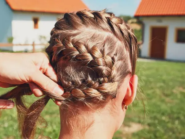 Zopf flechten für Oktoberfest Frisuren einfach. Eine Hand flechtet das braune Haar zu einem kunstvollen Zopf.